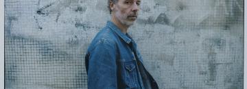 Le chanteur Baxter Dury se tient de profil, il porte une veste en jean.