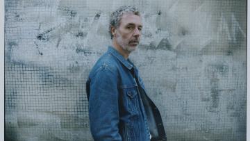 Le chanteur Baxter Dury se tient de profil, il porte une veste en jean.