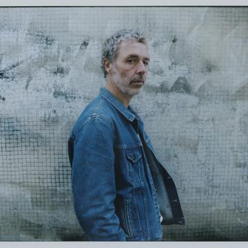 Le chanteur Baxter Dury se tient de profil, il porte une veste en jean.