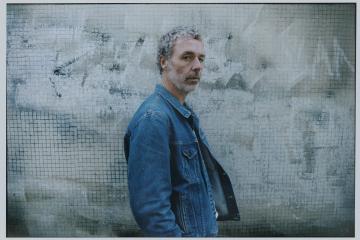 Le chanteur Baxter Dury se tient de profil, il porte une veste en jean.